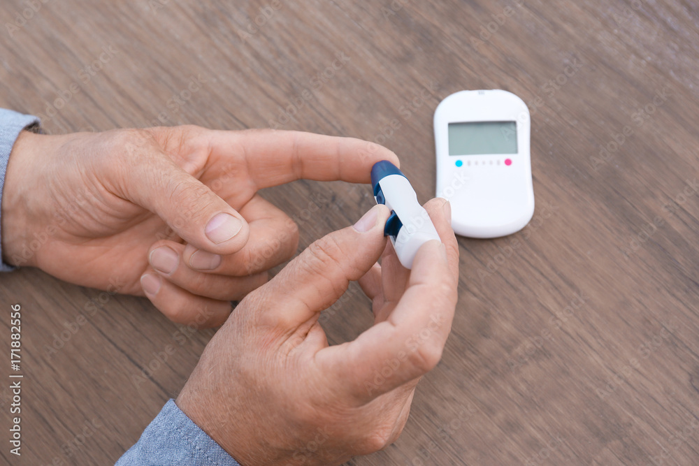 Man taking blood sample with lancet pen on wooden background Man taking blood sample with lancet pen on wooden background