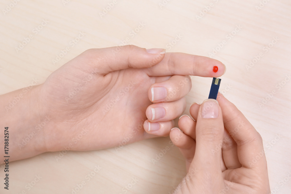 Woman using test strip for glucose level on wooden background Woman using test strip for glucose level on wooden background