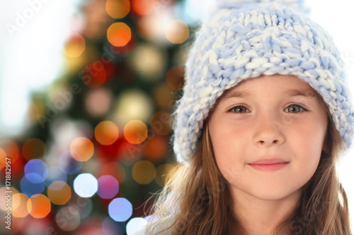 Happy little girl in hat against blurred Christmas tree