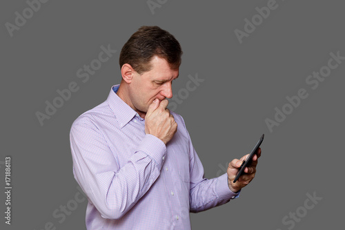 Photos The adult man looks anxiously at the mobile device, holding his hand near his face