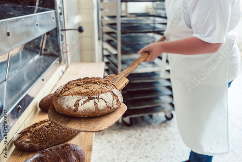 Photos Bäcker Frau in Backstube legt Brot auf Brett ab
