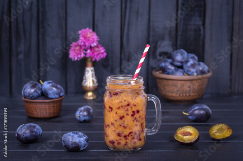 Plum smoothies and raw plums on black wooden background