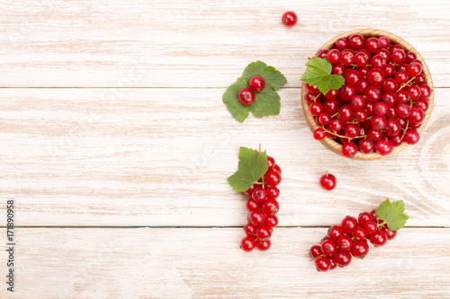 Red currant berries in a wooden bowl with leaf on the light wooden background with copy space for your text. Top view