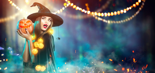 Halloween. Witch with a carved pumpkin and magic lights in a dark forest