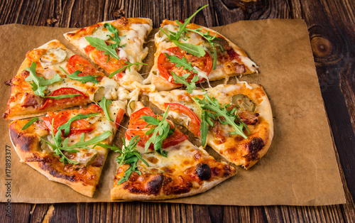 Homemade pizza with tomatoes, cheese, meat and herbs. Pizza on a wooden background. Restaurant meal. Copy space.