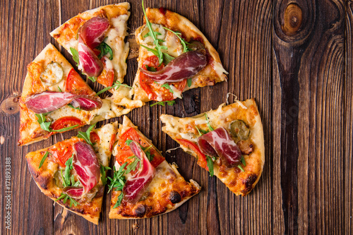 Homemade pizza with tomatoes, cheese, meat and herbs. Pizza on a wooden background. Restaurant meal. Copy space.