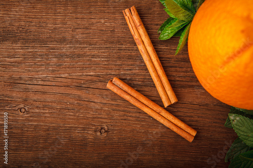 Fresh orange with cinnamon, mint and melissa on a wooden background. Close-up. Top view. Space for text. Background