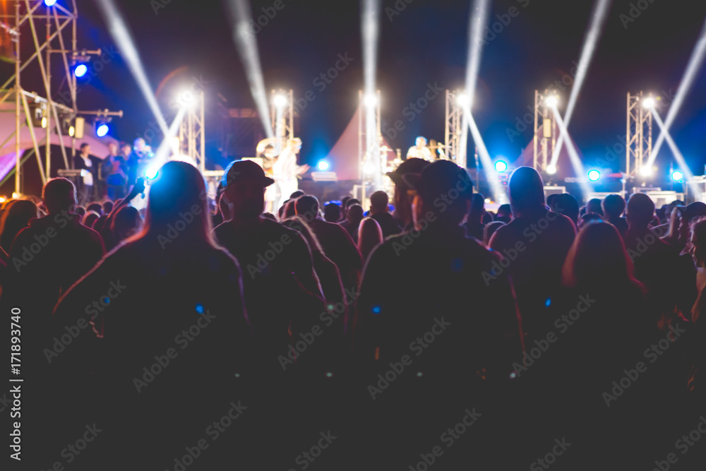 silhouettes of concert crowd in front of bright stage lights. Stage lights. Night party. Festival. Rock concert. Outdoor festival night party time.