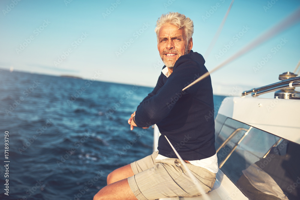 Fototapeta premium Mature man sitting on his sailboat looking at the ocean