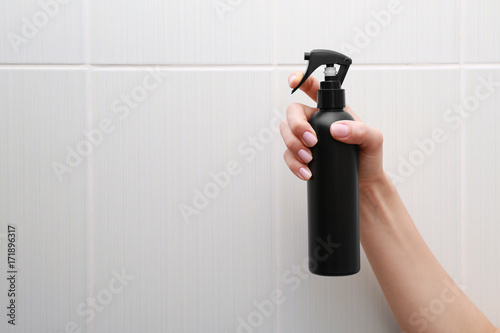 Young woman holding bottle with spray for hair on tile wall background