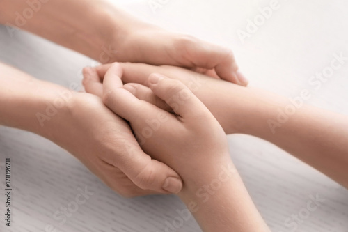 Mother and daughter holding hands together on light background, closeup