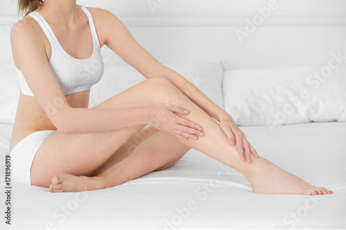 Young woman touching her leg on bed