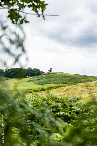 A old and medieval tower at the top of a beautiful green grass covered hill on a cloudy day at Bradgate Park, Leicester, England photo