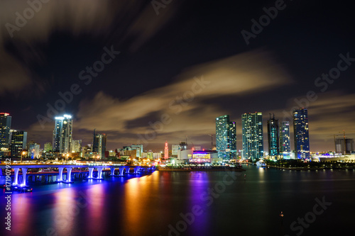 Miami city skyline panorama at dusk with urban skyscrapers and bridge over sea with reflection