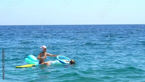 Youngs relaxing on a blue inflatable mattress with ocean sunset reflection