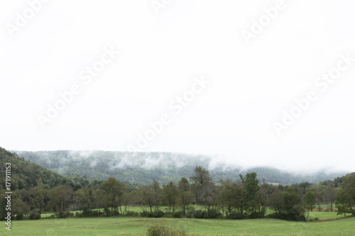 View of cloud draped mountain with fog and green fields below 