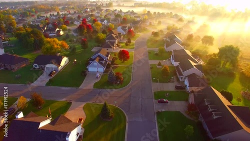 Tranquil idyllic Autumn neighborhood houses shrouded in fog at daybreak, Fall colors, aerial flyover. photo