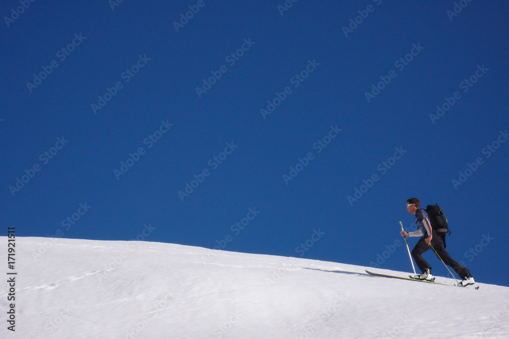 single young male back country skier hiking up a snowy ridge of a mountain in the Swiss Alps near Sargans in winter underneath a clear blue sky
