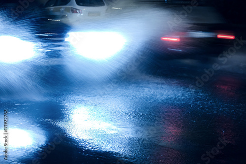 blurred car headlight shining through rain water splashes at night