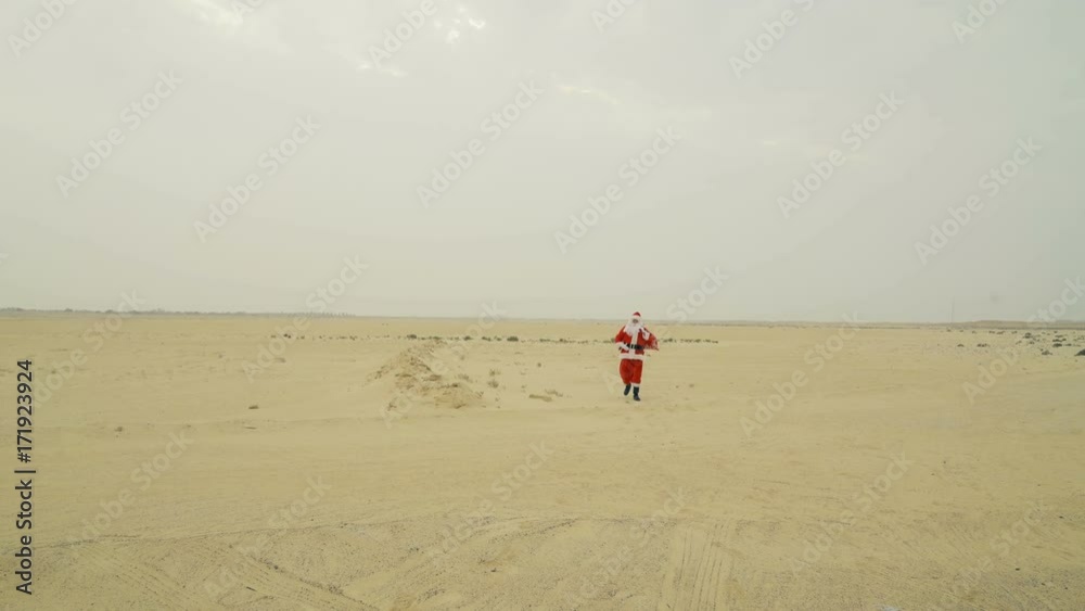 Santa claus with sack of presents is coming to town from the desert. Santa walks on sand in desert, found asphalt road, looking for a city Santa claus with sack of presents is coming to town from the desert. Santa walks on sand in desert, found asphalt road, looking for a city