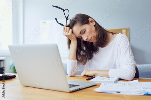 tired young office worker at desk while trying to work in modern office photo