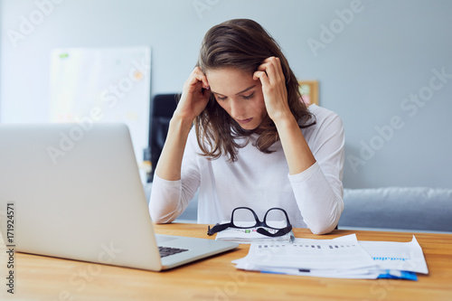 Beautiful stressed young entrepreneur holding her head and looking down stress and headache in office