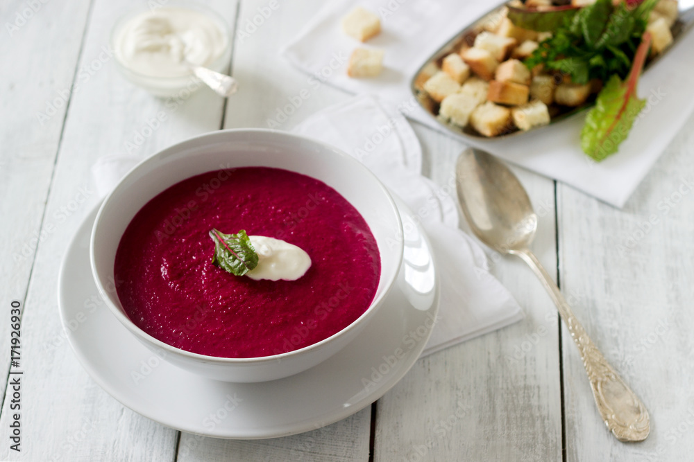 Beet cream soup with sour cream and croutons and a white plate. Rustic style, selective focus.