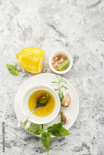 Ingredients for homemade lemon sauce vinaigrette dressing for salad with olive oil, salt, pepper, lemon, lemon zest, juice, garlic and herbs to taste. Top view on a light background. photo