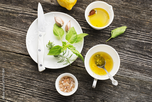 Ingredients for homemade lemon sauce vinaigrette dressing for salad with olive oil, salt, pepper, lemon, lemon zest, juice, garlic and herbs to taste. Top view on a wooden background.