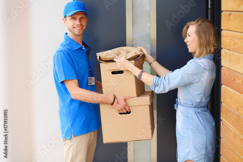 Smiling delivery man in blue uniform delivering parcel box to recipient - courier service concept. Smiling delivery man in blue uniform © lenets_tan