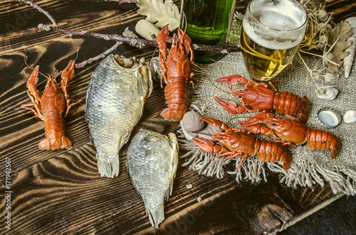 Salted boiled red crayfish with dried salted fish,glass with beer and a bottle of beer on canvas lying on dark wooden boards