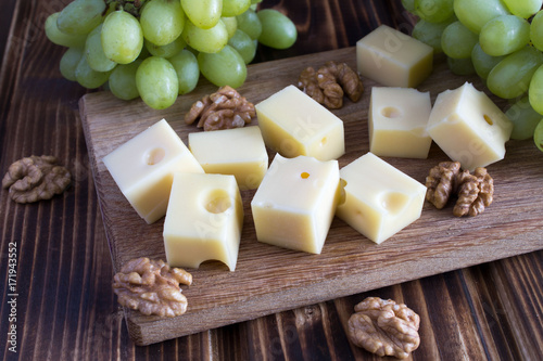 Pieces of cheese,nuts and  green grapes on the brown cutting board