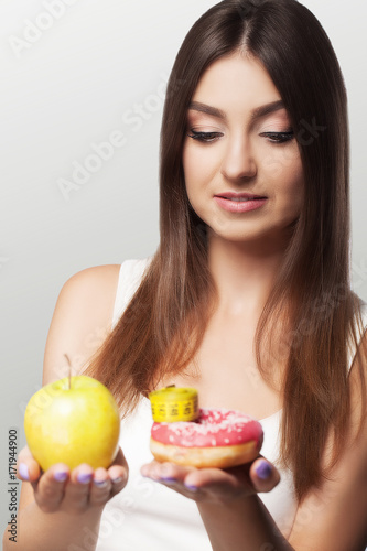 A young woman makes a choice between healthy and harmful food. Sport. Diet. The concept of health and beauty. On a gray background.