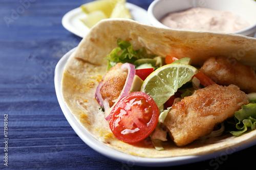 Plate with tasty fish taco and sauce on wooden table