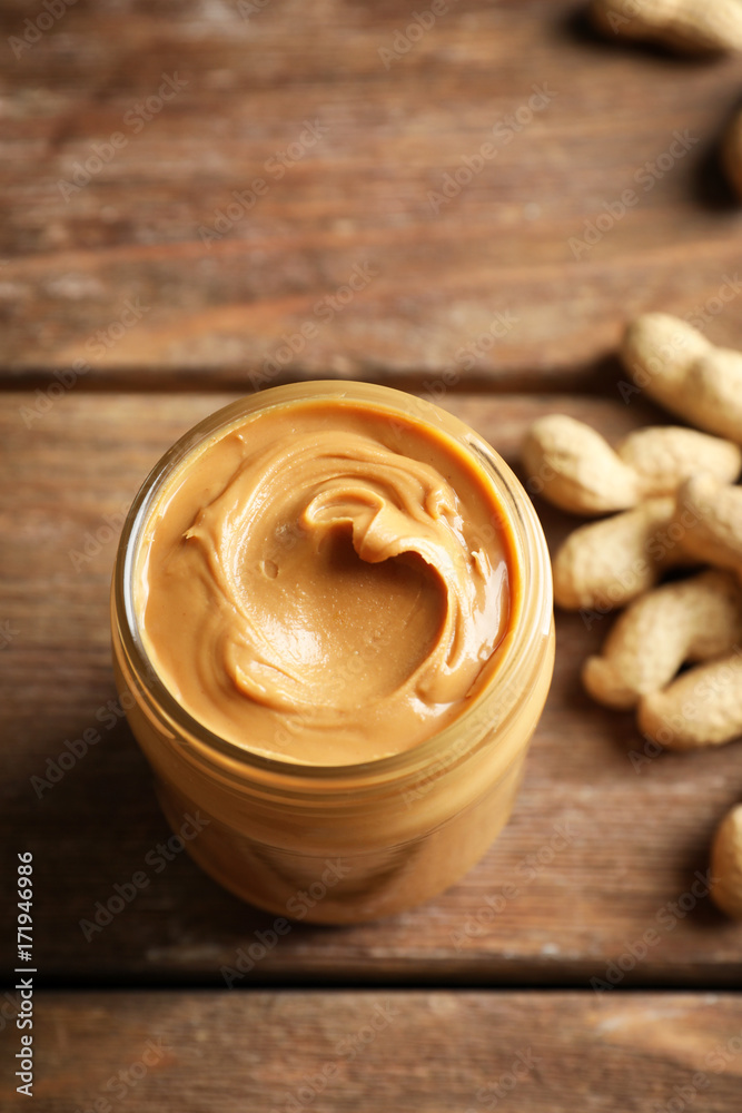 Glass jar with creamy peanut butter on wooden background Glass jar with creamy peanut butter on wooden background