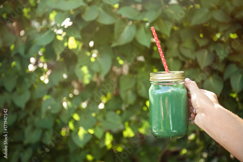 Female hand holding jar with fresh green smoothie outdoors