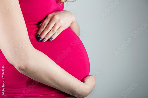 Wallpaper Mural Young beautiful pregnant girl in pink tshirt hugs her belly with her hands on gray background, horizontal image Torontodigital.ca