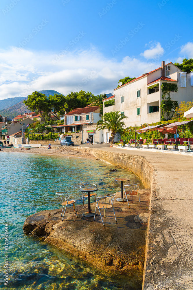 Naklejka premium Chairs with tables of coastal bar on rocks and view of shore in Bol town, Brac island, Croatia.