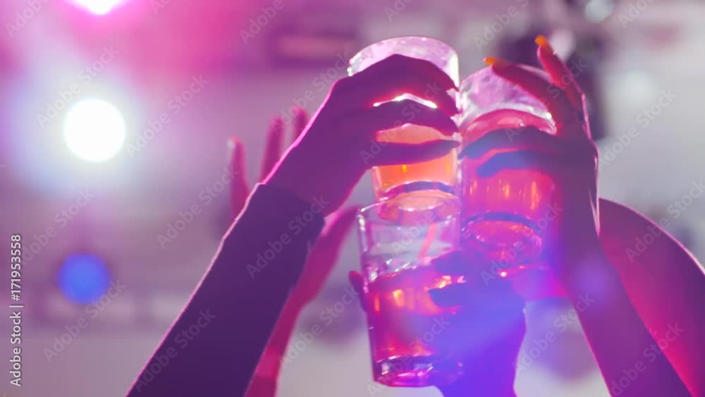 hands crowd raising glasses to make toast with cocktails at night club, arms toasting with beverage on party in lumiere lights, friends do toasts at night party in slow motion