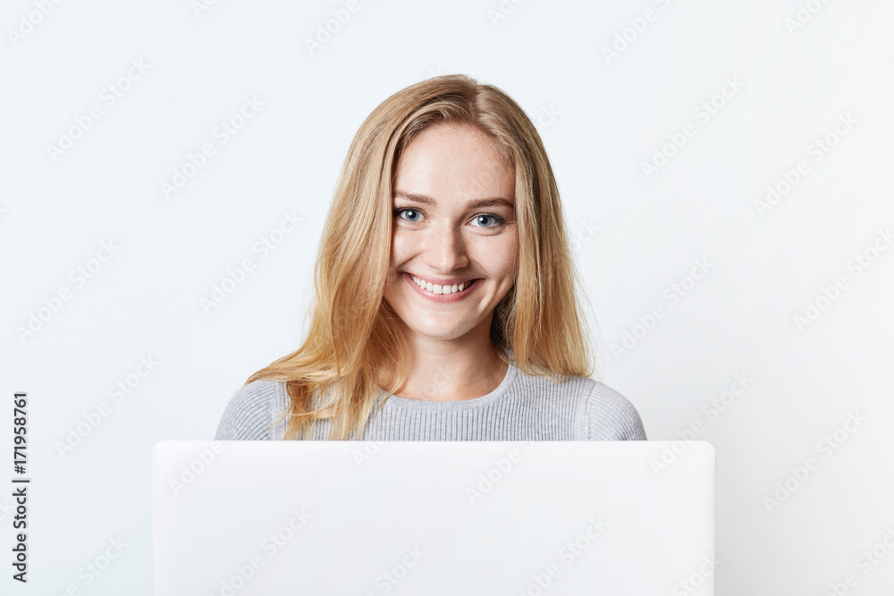 Happy smiling self-employed woman works at home, sits in front of opened laptop, enjoys free wireless internet connection. Lovely teenage girl messages with friends, has pleasant smile on face Happy smiling self-employed woman works at home, sits in front of opened laptop, enjoys free wireless internet connection. Lovely teenage girl messages with friends, has pleasant smile on face