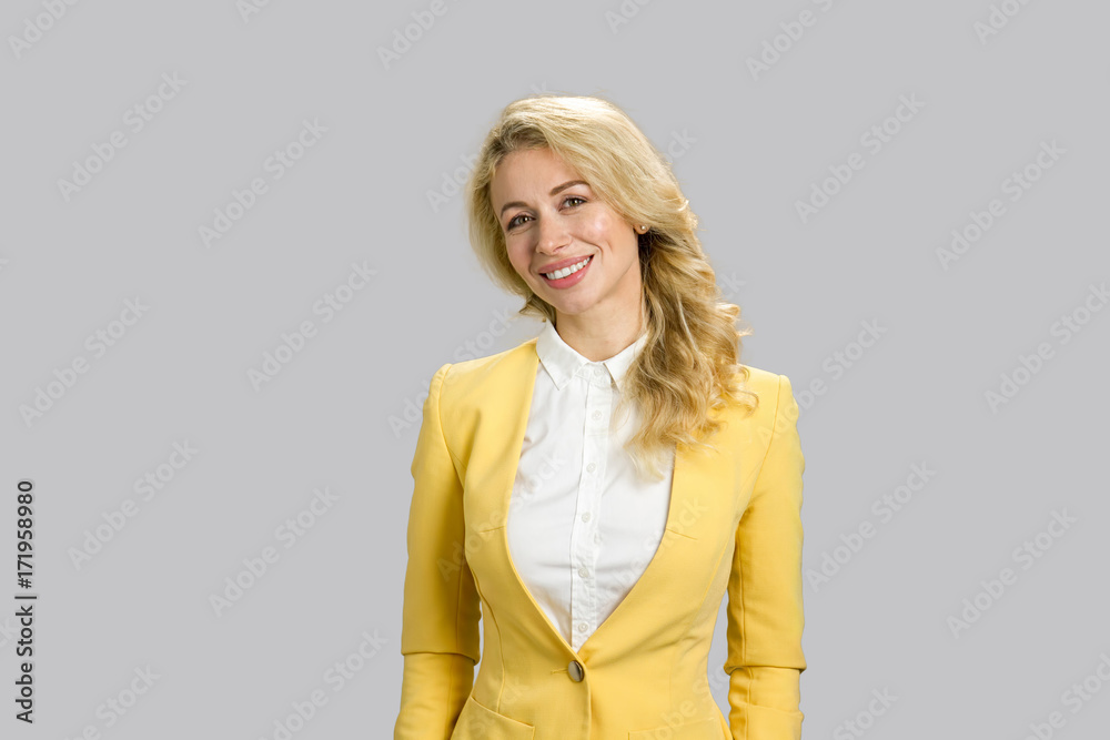 Portrait of smiling young business woman. Blond lady in yellow jacket and white shirt smiling on grey background. Portrait of smiling young business woman. Blond lady in yellow jacket and white shirt smiling on grey background.