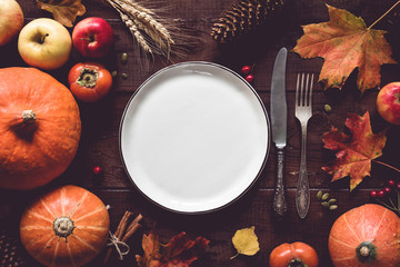 Autumn or thanksgiving day table setting. Fallen leaves, pumpkins, spices, empty plate and vintage cutlery on wooden table. Top view, toned image