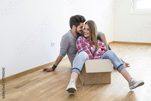 Young couple in new appartment sitting on the floor, she is on the box