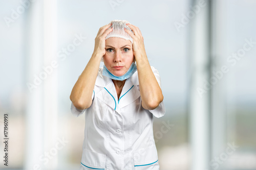 Surprised and confused female doctor. Portrait of white-skin female doctor or nurse surprised starring with scared eyes, blurred background.