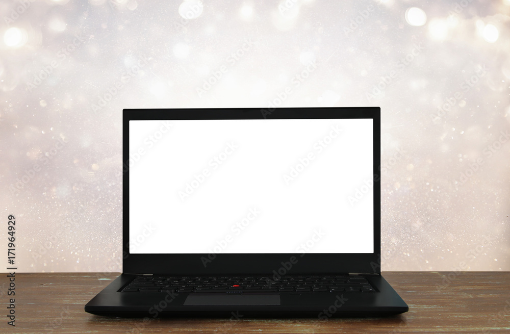Fototapeta premium open laptop with white screen on wooden table in front of abstract glitter background