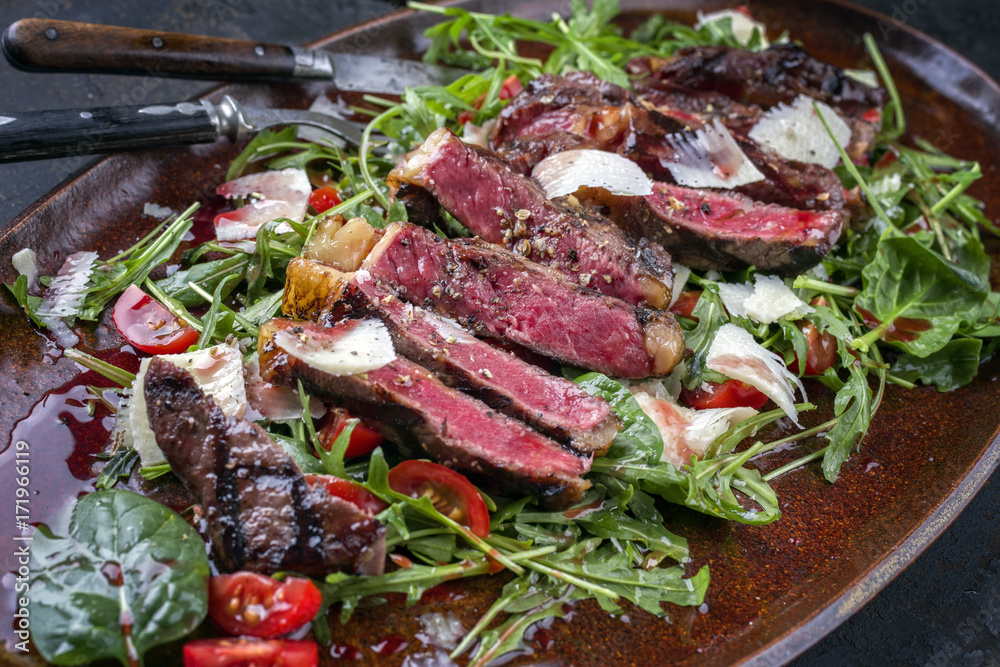 Traditional Italian tagliata steak with parmesan and salad as close-up on a plate