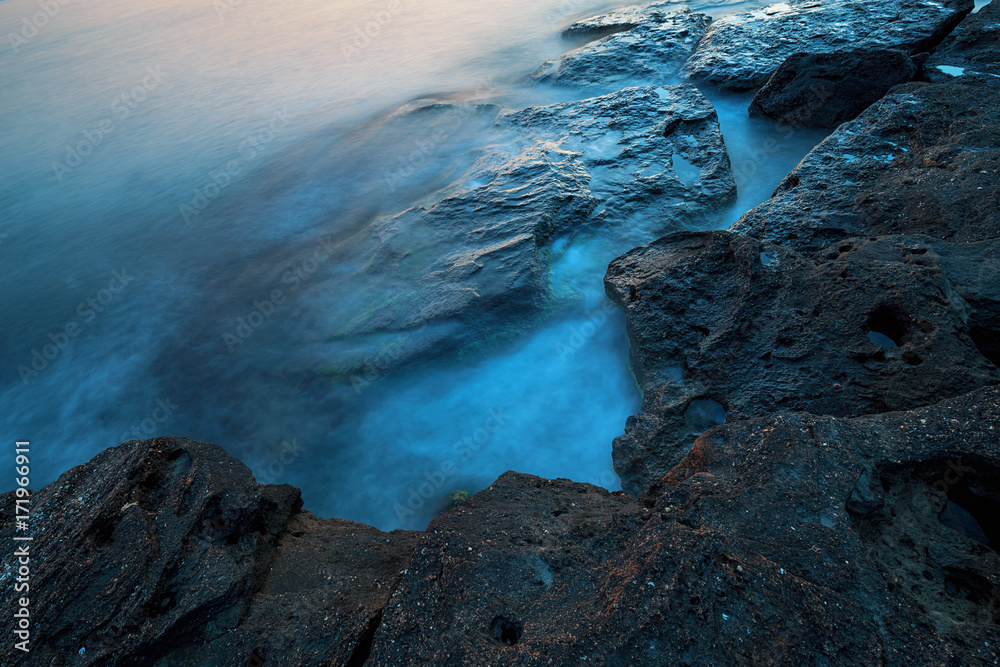 Beautiful mysterious marine landscape at sunset. Volcanic reef and ocean
