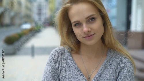 close-up of a young attractive blonde woman. the girl is looking at the camera and smiling. touches the hair. long, long look into the camera. behind the beautiful old Uski streets of Art Nouveau photo