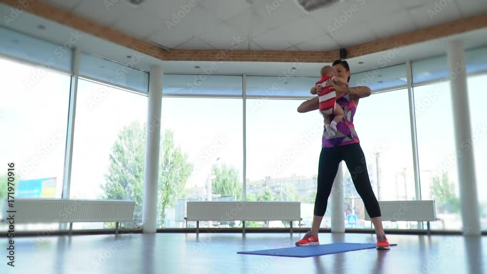 A woman in sports is engaged in sports with her young child in a gym with a view of the city, slow motion A woman in sports is engaged in sports with her young child in a gym with a view of the city, slow motion
