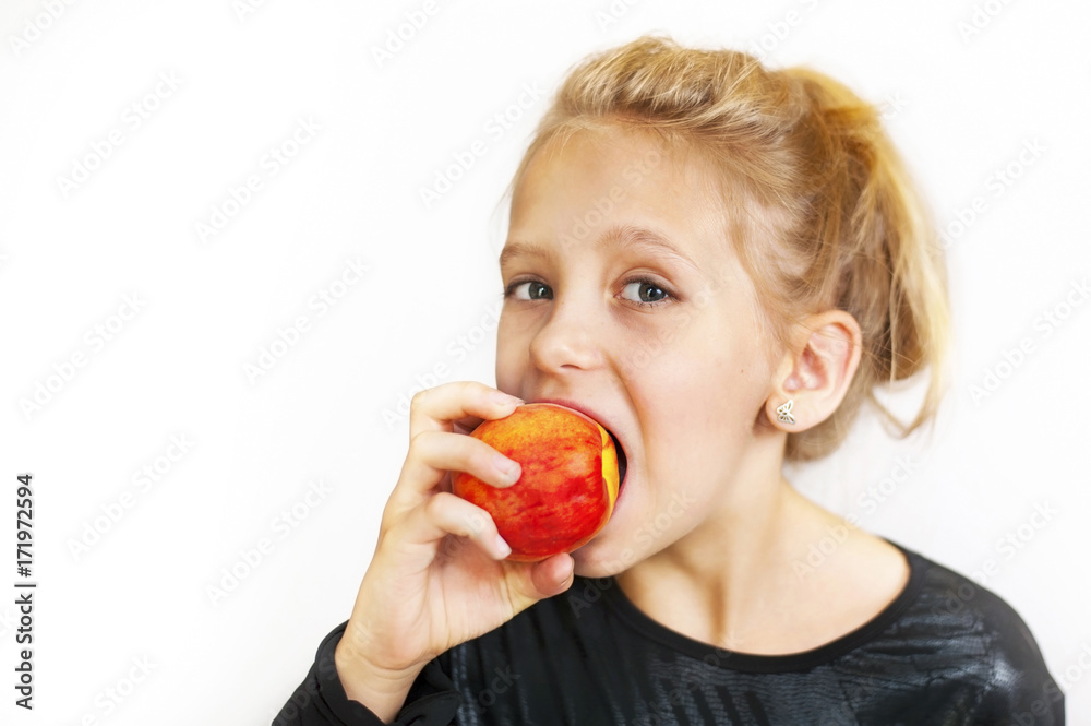 The young girl eats a delicious peach and smiles The young girl eats a delicious peach and smiles